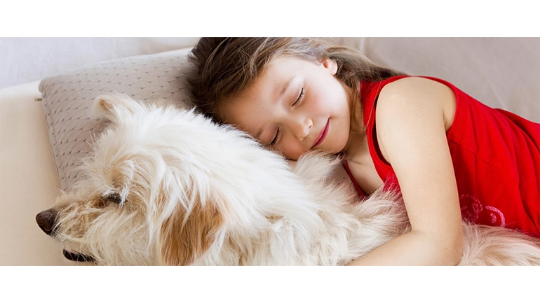 Απεικονίζεται ένα κοριτσάκι να κοιμάται με τον σκύλο της αγκαλιά.